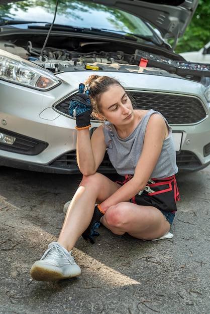 Frau mit Arbeitswerkzeugen, die neben einem kaputten Auto steht und auf Hilfe wartet