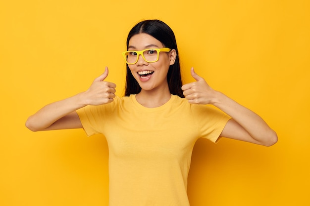 Frau mit asiatischem Aussehen in gelben T-Shirts mit Brille, die den gelben Hintergrund der Mode unverändert aufwirft