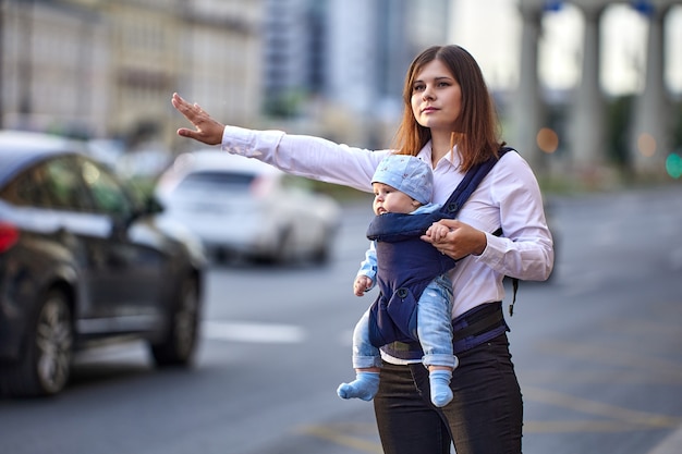 Frau mit Baby im Tragetuch hält Taxi beim Gehen an