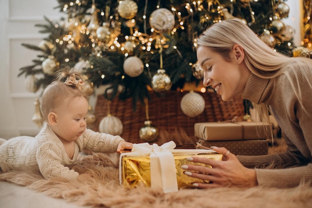 Frau mit Babytochter hält Weihnachtsgeschenke am Weihnachtsbaum