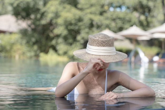 Frau mit Bikini und Strohhut bedeckt Gesicht im Pool entspannen. Spa-Behandlungskonzept.