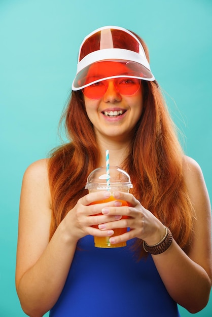 Frau mit blauem Badeanzug, Hut und Sonnenbrille trinkt Fruchtsaft aus einer Tasse