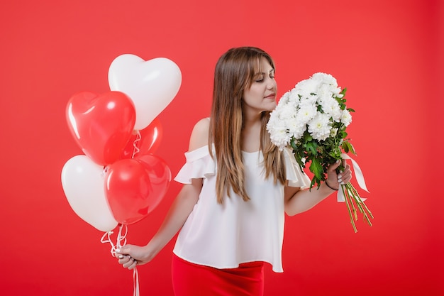 Frau mit Blumenstrauß der weißen Blume und Herz formten die Ballone, die auf roter Wand lokalisiert wurden