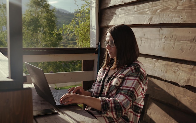 Frau mit Brille, die draußen auf der Terrasse am Computer arbeitet
