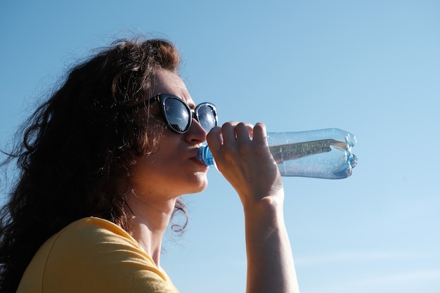 Frau mit Brille trinkt bei heißem Wetter Wasser aus einer Flasche