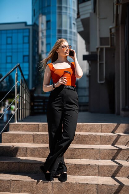 Frau mit Brille und klassischer Markenkleidung, die eine Tasse Kaffee hält und auf City lächelt