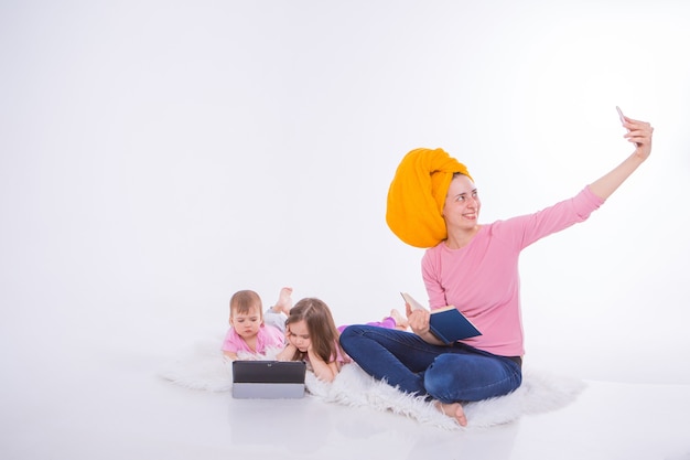 Frau mit Buch in ihren Händen spricht am Telefon. Kinder sehen Cartoon auf ihrem Tablet. Mutter wusch sich die Haare. Handtuch auf dem Kopf. Hobbys und Erholung mit Gadgets.