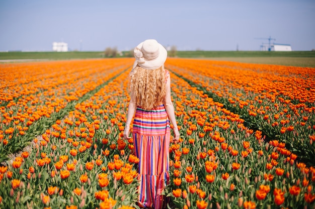 Frau mit dem langen roten Haar, das ein gestreiftes Kleid bereitsteht die Rückseite auf buntem Tulpenfeld trägt.