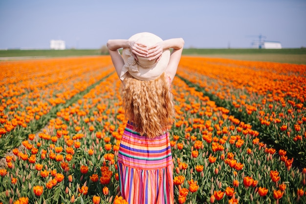 Frau mit dem langen roten Haar, das ein gestreiftes Kleid bereitsteht die Rückseite auf buntem Tulpenfeld trägt.