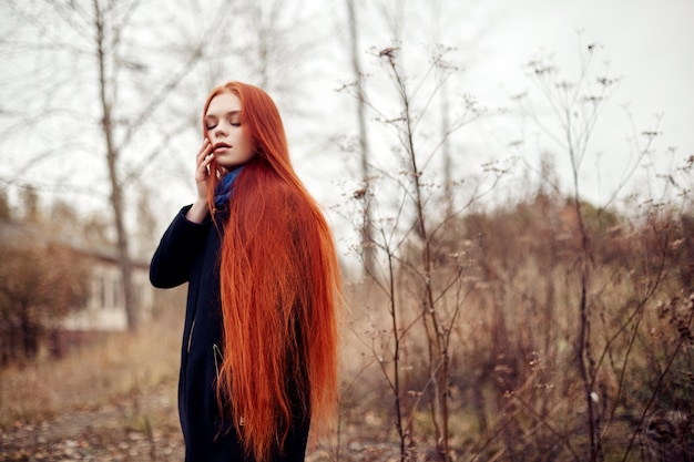 Frau mit dem langen roten Haar geht in Herbst auf Straße