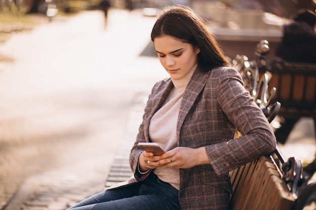 Frau mit dem Telefon, das auf einer Bank sitzt