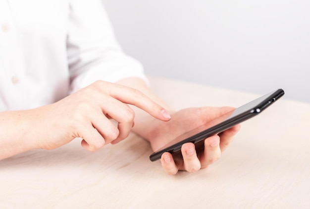 Frau mit dem Zeigefinger, die am Telefon auf die Schaltfläche „OK“ klickt. Frau, die am Tisch sitzt und ein Smartphone hält, um mit sozialen Medien im Internet zu surfen