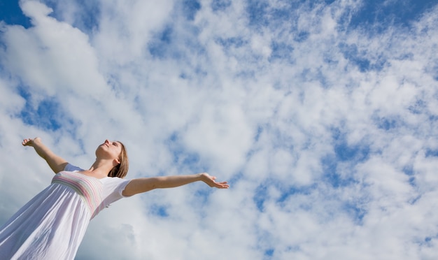 Frau mit den Armen streckte gegen blauen Himmel und Wolken aus