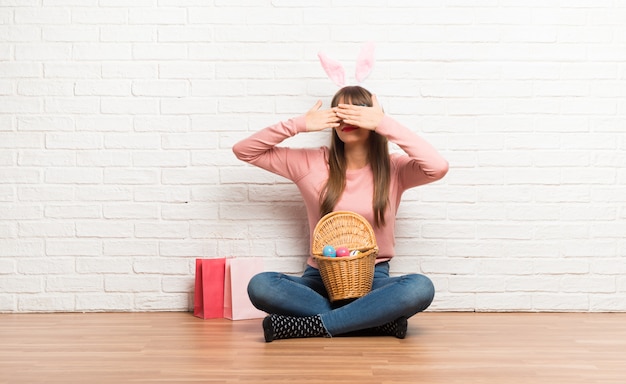 Frau mit den Häschenohren für Osterferien sitzt auf dem Bodenbelag mit den Augen