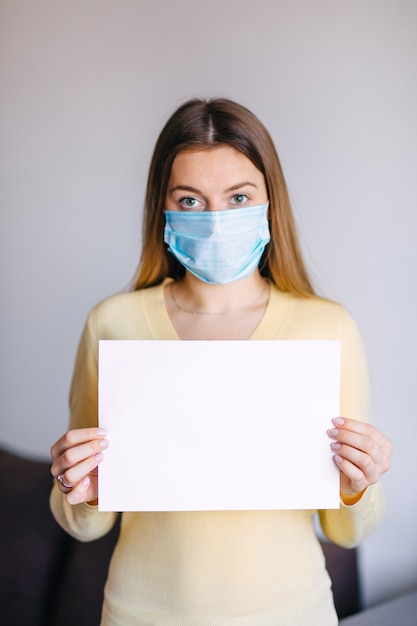 Foto frau mit der chirurgischen maske hält leeres papier