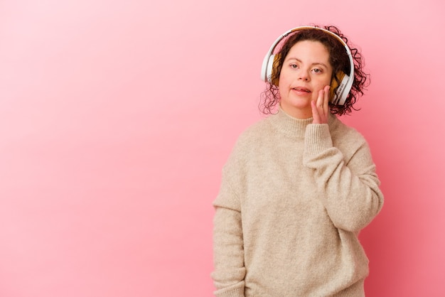Frau mit Down-Syndrom mit Kopfhörern, die auf rosa Wand isoliert werden, sagt eine geheime heiße Bremsnachricht und schaut zur Seite