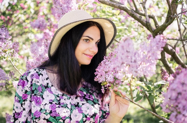 Frau mit dunklem Haar in einem Strohhut in der Nähe von Kirschblüten im Frühling