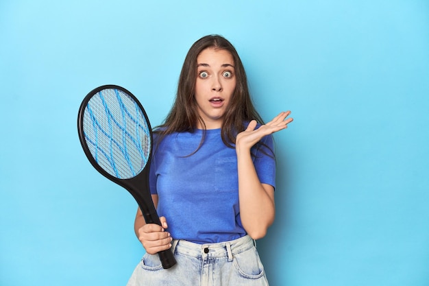 Frau mit einem elektrischen Bug-Zapper auf blauem Hintergrund überrascht und schockiert