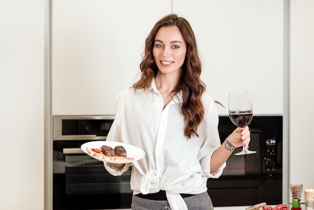 Frau mit einem Fleischteller und einem Rotwein an der Küche