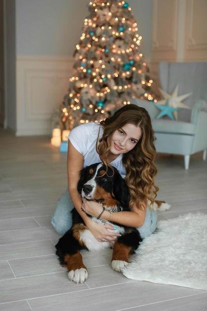 Frau mit einem großen Hund in der Silvesternacht auf dem Hintergrund des Zimmers mit einem Weihnachtsbaum