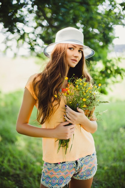 Frau mit einem Hut hält Blumen