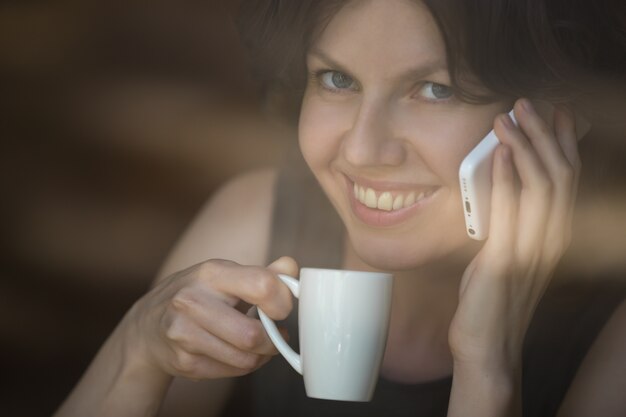 Frau mit einem Kaffee und am Telefon sprechen