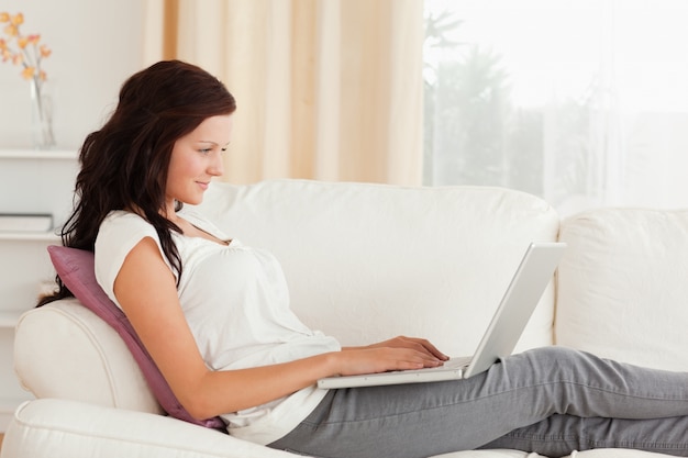 Frau mit einem Laptop, der auf einem Sofa liegt