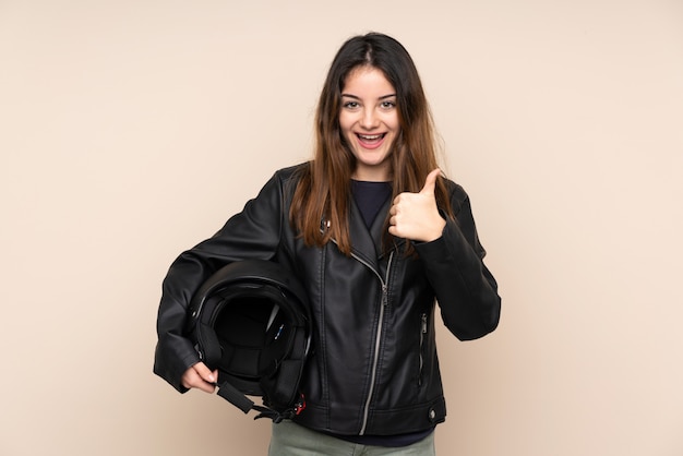 Frau mit einem Motorradhelm auf beige Wand, die eine Daumen hoch Geste gibt