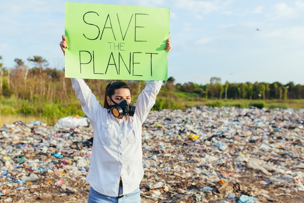 Foto frau mit einem poster rettet den planeten, streikposten müllverseuchte umgebung, brennendes feuer und schwarzer rauch