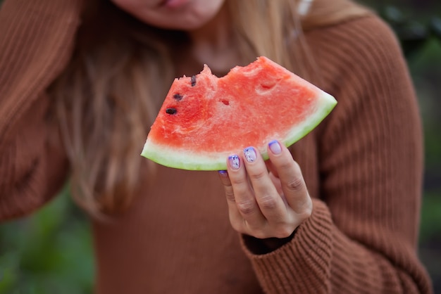 Frau mit einem Stück reifer Wassermelone in einem Garten