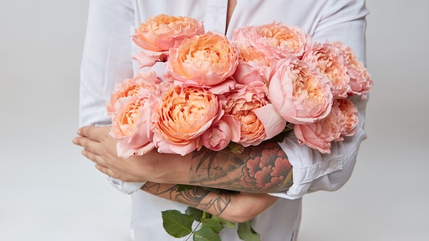 Frau mit einem Tattoo auf den Händen hält einen Strauß rosa Rosen, Valentinstag