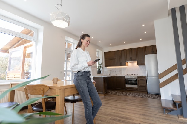 Frau mit einem Telefon in ihrem Wohnzimmer. Moderne Wohnzimmereinrichtung im skandinavischen minimalistischen Stil
