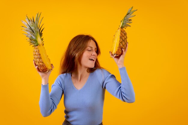 Frau mit einer Ananas in Sonnenbrille tanzt und ist glücklich mit der Ananas, die auf halbgelbem Hintergrund geschnitten ist