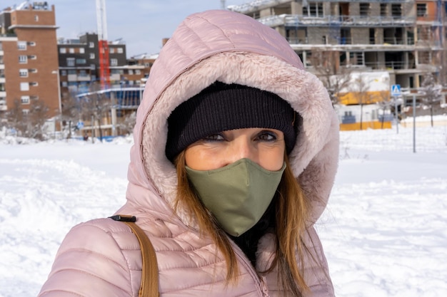 Frau mit einer Gesichtsmaske, die an einem Wintertag im Freien in die Kamera blickt