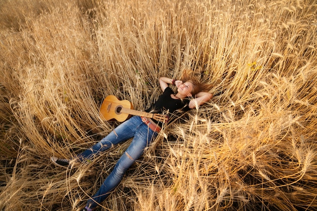 Foto frau mit einer gitarre, die auf dem weizengebiet liegt