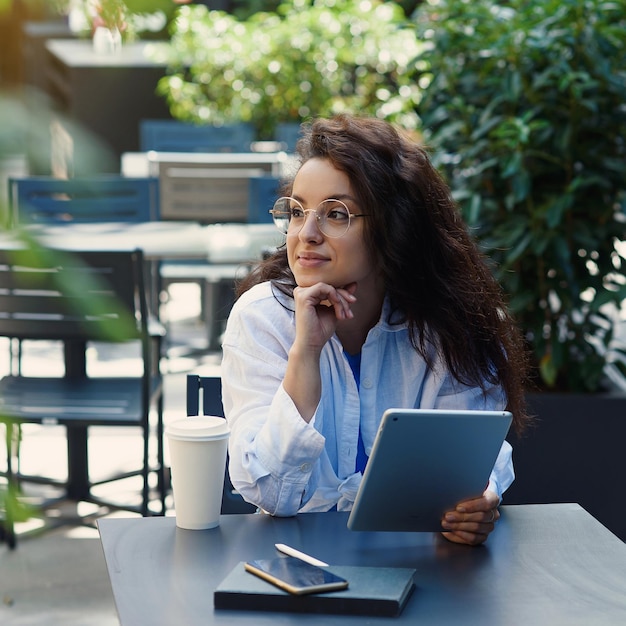 Frau mit einer Tasse Kaffee, die morgens im Café im Freien arbeitet