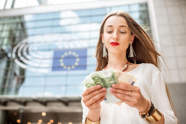 Frau mit Euro-Banknoten vor dem Parlamentsgebäude der Europäischen Union in Brüssel