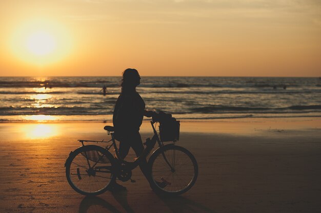 Frau mit Fahrrad am Strand bei Sonnenuntergang