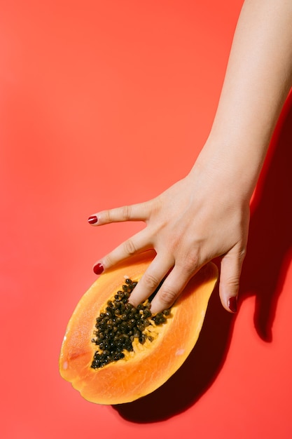 Frau mit Fingern auf frischer Papaya mit schwarzen Samen. Erotisches Konzept