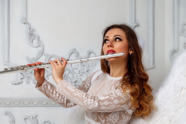 Frau mit Flöte und Flügeln. Mädchenschauspielerin im Anzug mit Flügeln und Flötensitzen. Strukturierte Wand im Hintergrund. Das Konzept der musikalischen Gestaltung. Platz für Ihren Schriftzug oder Ihr Logo