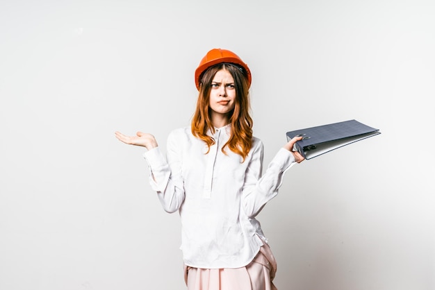 Frau mit gebautem helm hält dokumente in der hand und hat ein verwirrendes gesicht