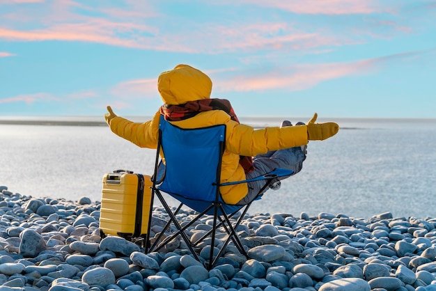 Frau mit gelbem Koffer entspannt sich allein auf Liegestühlen am Meer Travel Lifestyle-Konzept