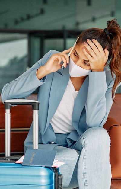 Foto frau mit gepäck am flughafen, das während der pandemie am telefon spricht