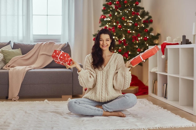 Frau mit Geschenkboxen mit Geschenken zu Hause in der Nähe von Weihnachtsbaum