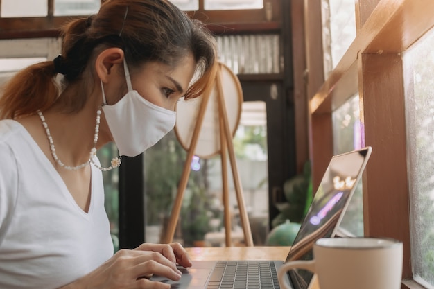 Frau mit Gesichtsmaske arbeitet am Laptop im Café