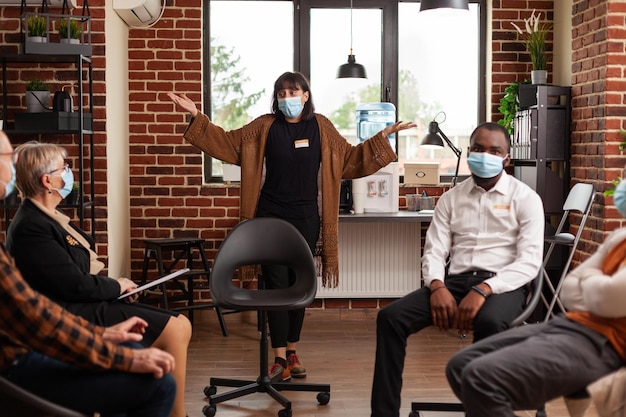 Frau mit Gesichtsmaske, die bei einem Gruppentreffen mit Leuten im Kreis über Probleme spricht. Person, die bei einer Therapiesitzung psychische Probleme ausdrückt, um Alkoholsucht zu heilen.