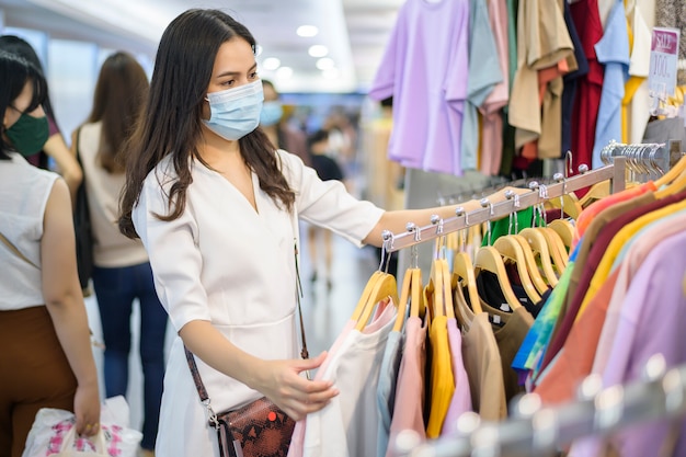 Frau mit Gesichtsmaske kauft Kleidung im Einkaufszentrum ein