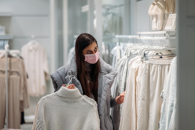 Frau mit Gesichtsmaske wählt Kleidung im Bekleidungsgeschäft aus