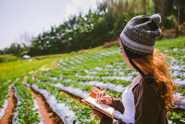 Foto frau mit gestrickter mütze, die auf dem feld steht und in einem buch schreibt