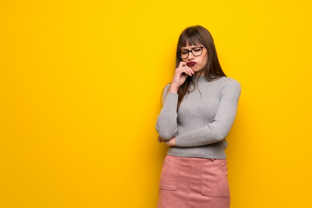 Frau mit Gläsern über der gelben Wand, die Zweifel hat